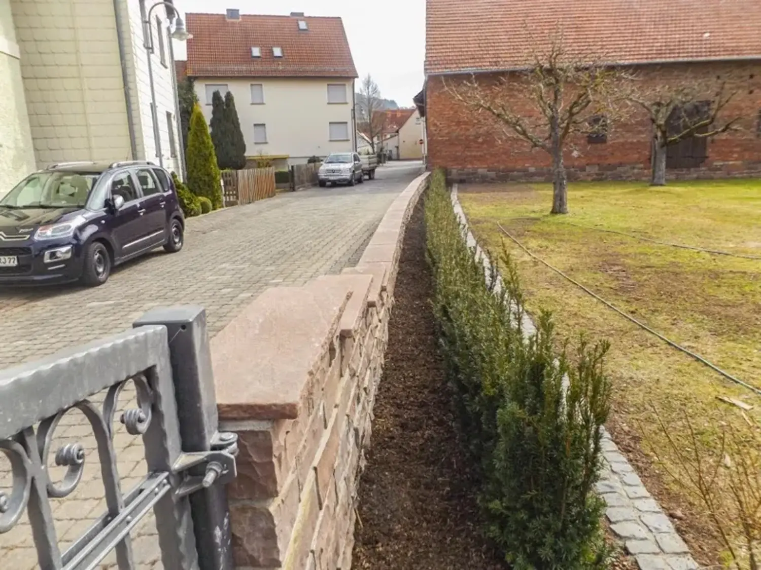 Gepflasterte Einfahrt mit geschnittener Hecke und Rasen