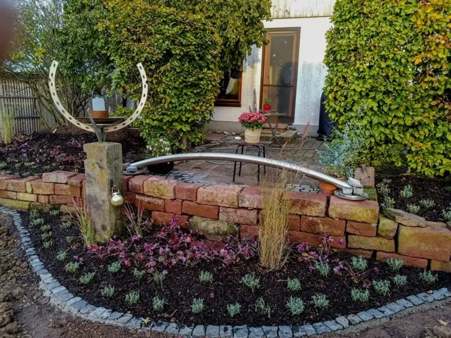 Garten mit runder Ziegelmauer, bepflanzt mit Blumen und Gräsern