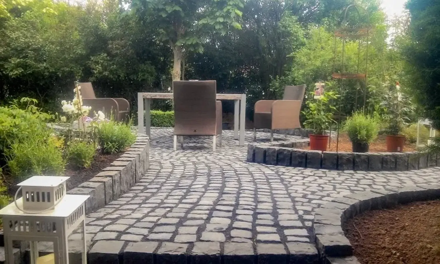 Gepflasterte Terrasse mit Tisch und Stühlen, umgeben von Pflanzen