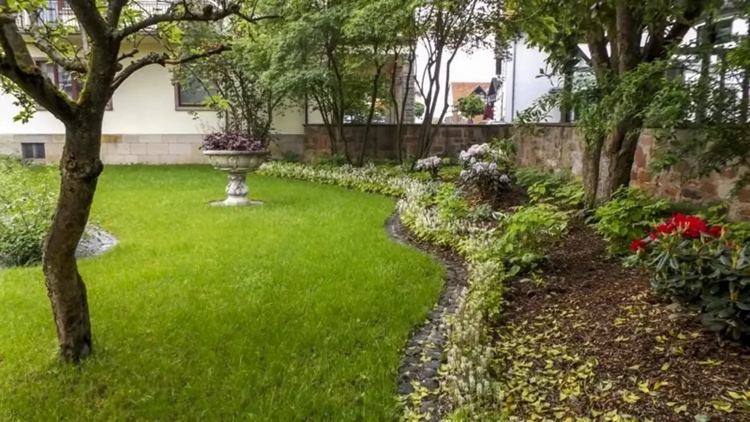 Gepflegter Garten mit grünem Rasen und steinernem Blumenkübel