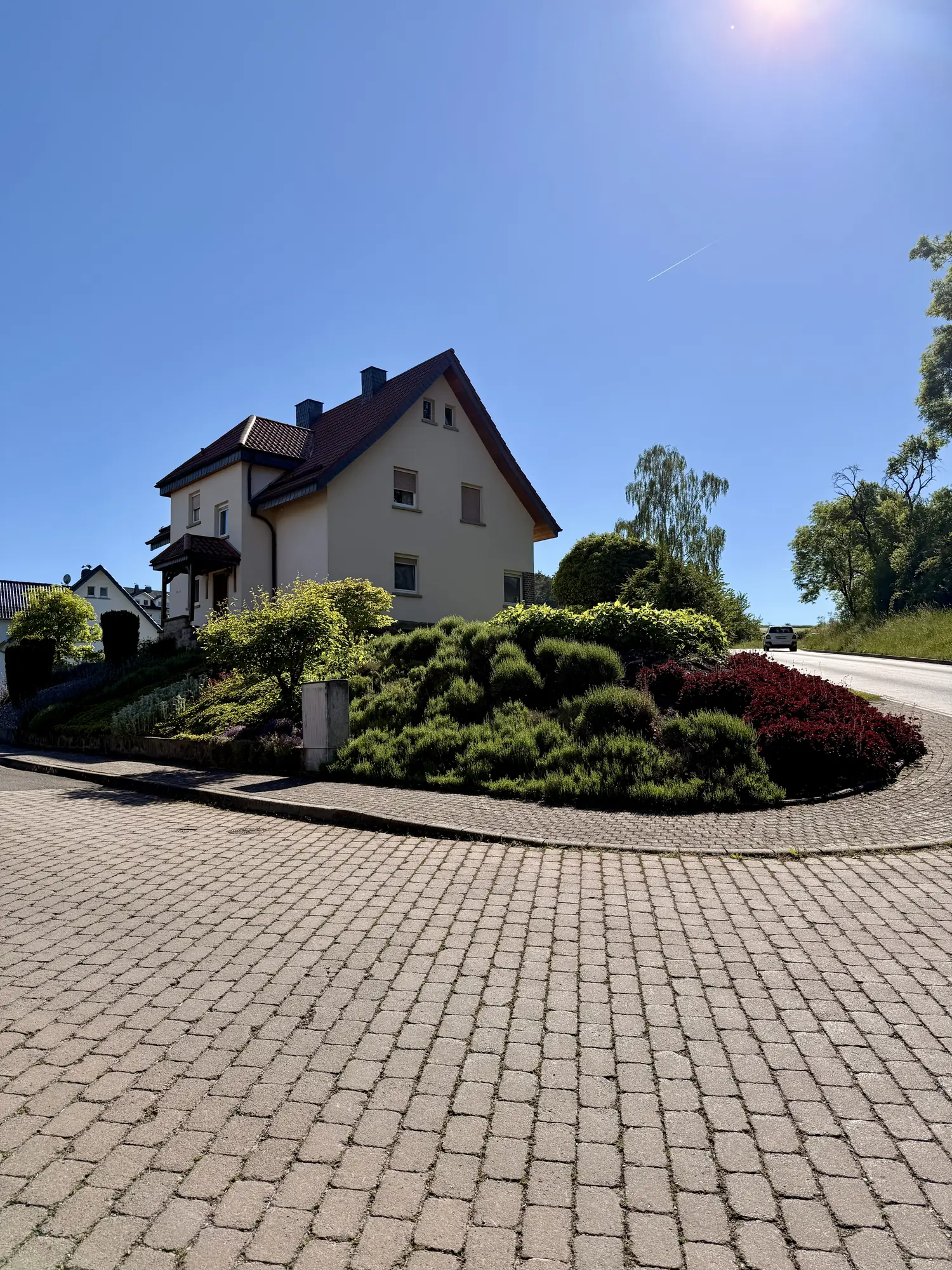 Von Brang Gartenbau gestaltete Hangbepflanzung mit geschwungener Pflasterfläche an einem Wohnhaus