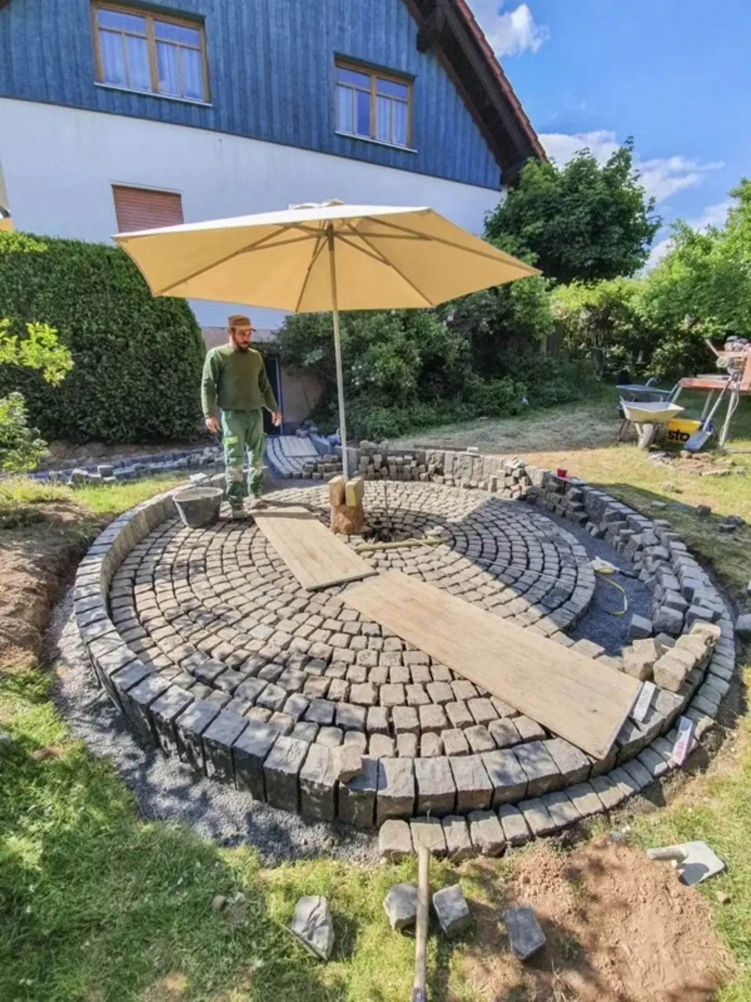 Dimitri Brang bei der Arbeit an einem runden Pflasterkreis unter einem Sonnenschirm