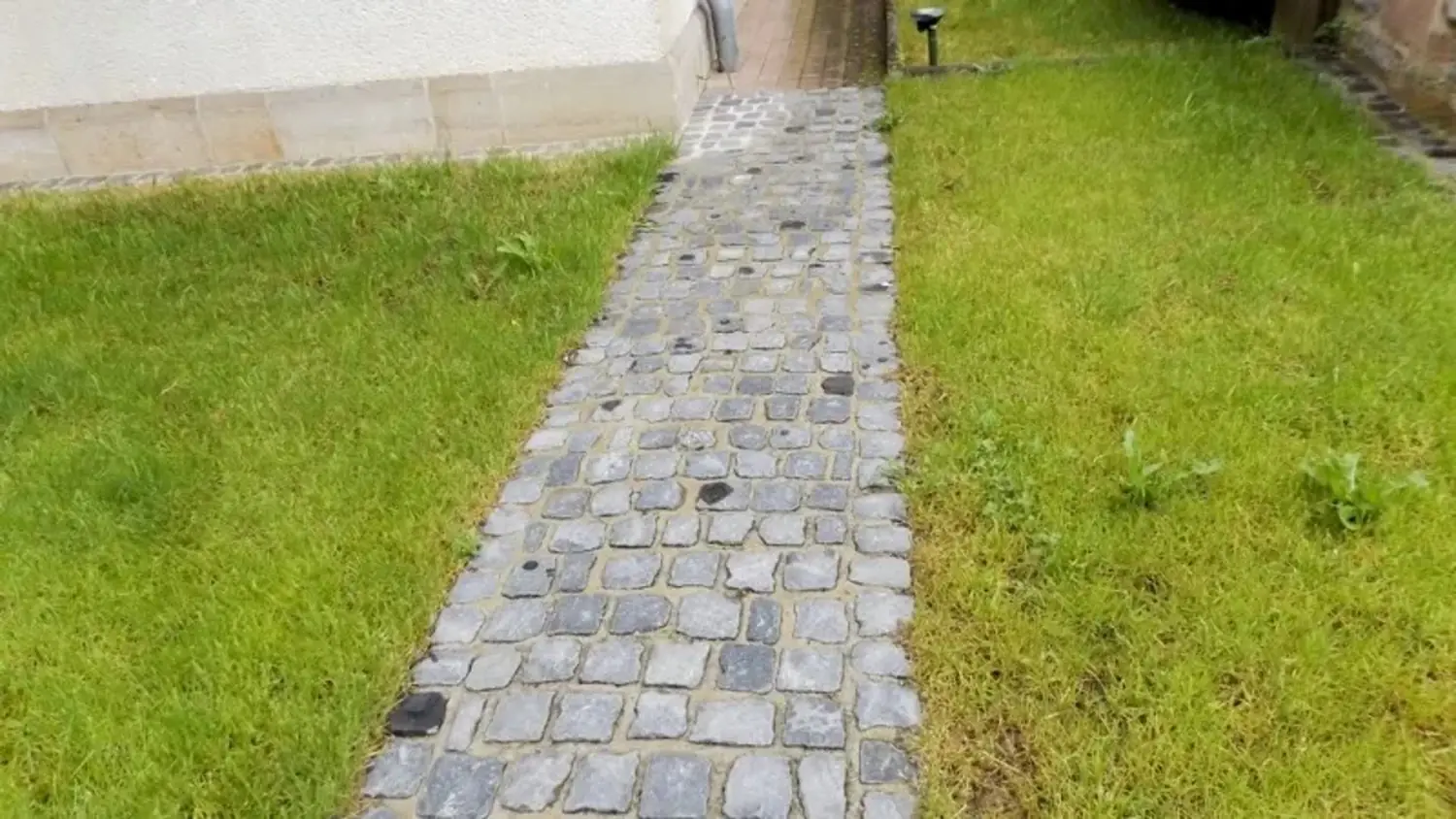 Schmaler gepflasterter Weg aus grauen Steinen im Rasen